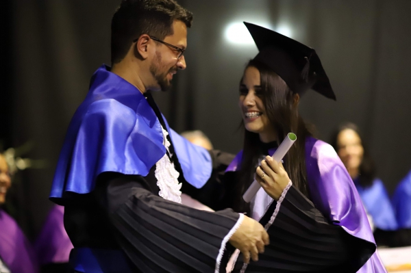 Imagem com um homem e uma mulher vestidos com beca e sorrindo